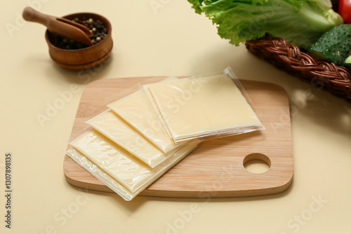 Board with slices of tasty processed cheese and bowl of peppercorns on beige background