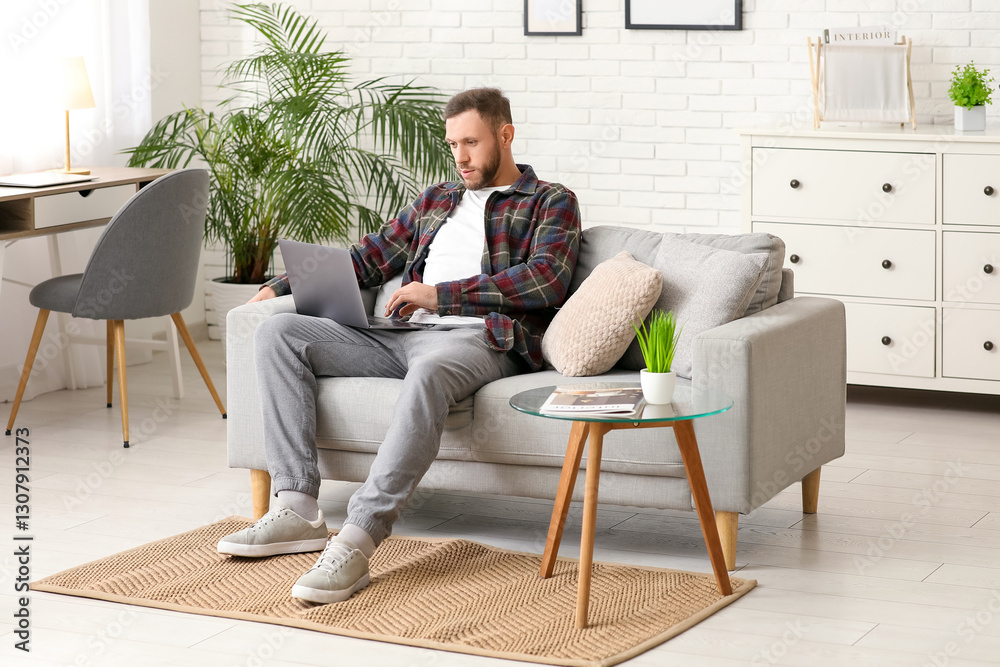 Handsome bearded man using laptop on grey sofa in living room Handsome bearded man using laptop on grey sofa in living room