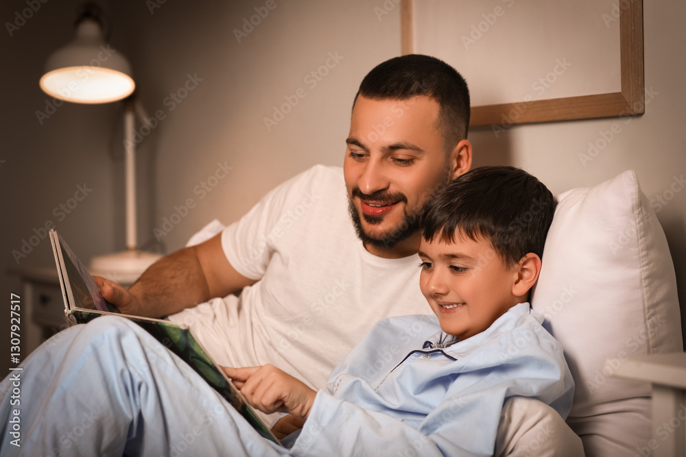 Fototapeta premium Young father and his little son reading book together in bed at home