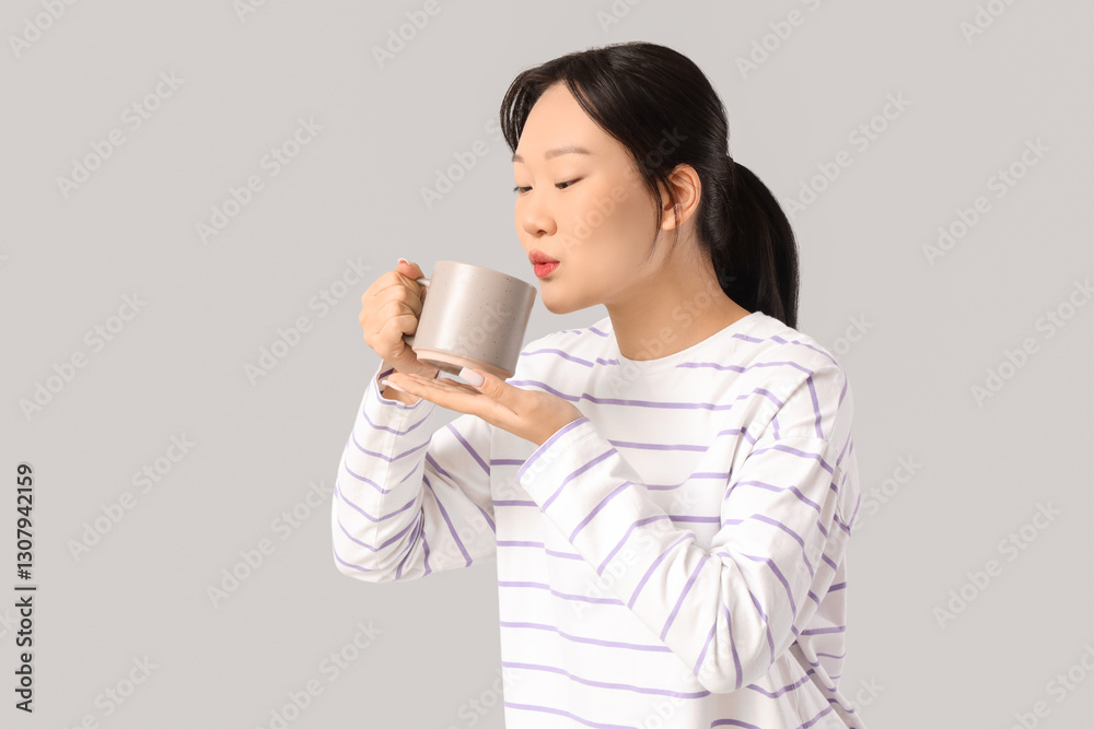 Young Asian woman drinking coffee from grey mug on grey background Young Asian woman drinking coffee from grey mug on grey background