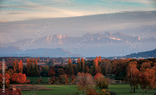 A view of the Alps in a light cloudy haze. Autumn trees in the foreground.