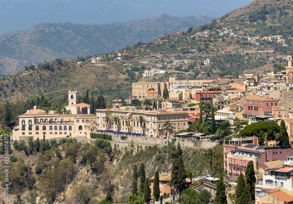 Naklejka premium Taormina, Sicily, Italy - July 5, 2024: Palaces and hotels on Via Roma seen from Ancient Greek theatre or Teatro antico. Cityscape and mountain landscape
