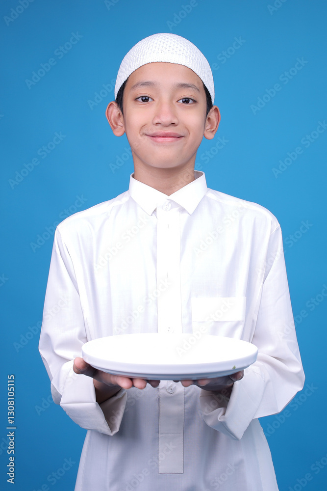 Young Asian Muslim Boy Showing Empty White Plate On Blue Background Young Asian Muslim Boy Showing Empty White Plate On Blue Background