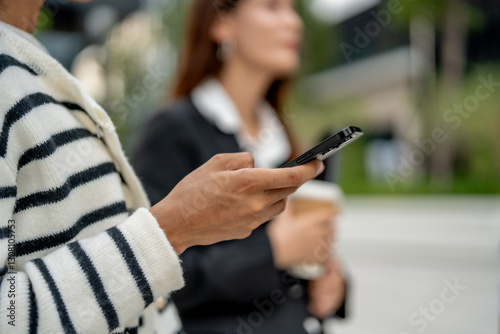 Wallpaper Mural woman holding smartphone while standing outdoors, dressed in striped sweater. She appears engaged with her device, showcasing modern urban lifestyle Torontodigital.ca