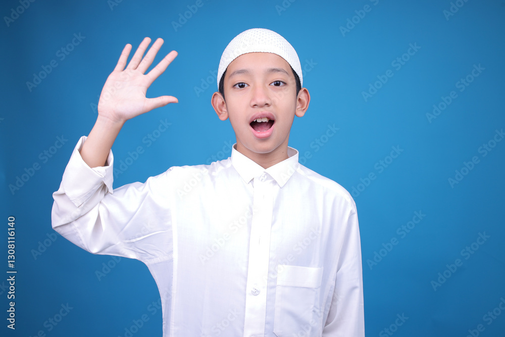 Cheerful Young Asian Muslim Boy Greeting By Waving Hand Over Blue Background Cheerful Young Asian Muslim Boy Greeting By Waving Hand Over Blue Background