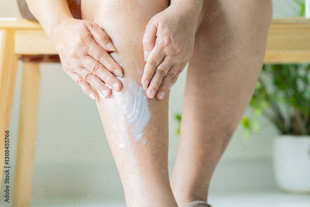 Cropped view of senior woman applying lotion on her leg while sitting on wooden chair at home. Cropped view of senior woman applying lotion on her leg while sitting on wooden chair at home.