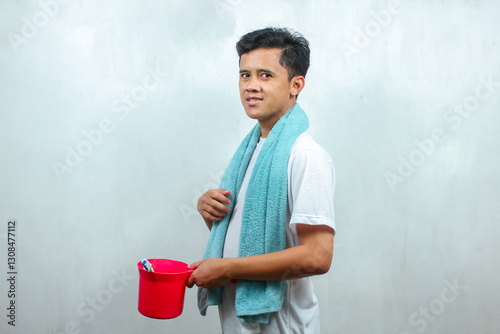 Asian man wearing white t-shirt carrying a ladle containing toiletries, isolated on white background photo