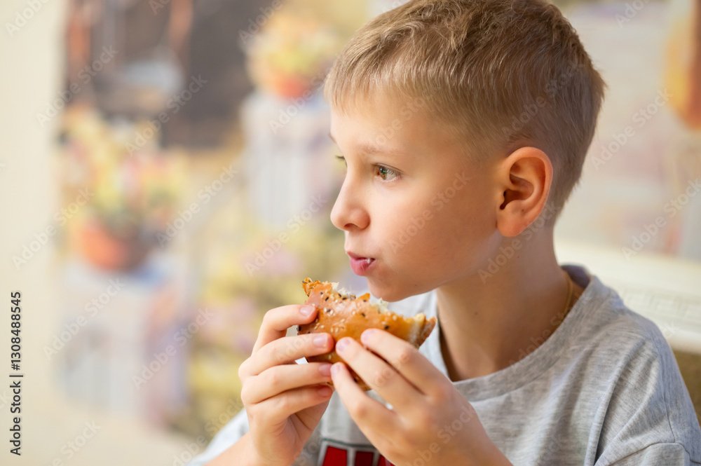 A young boy enjoys a delicious burger, taking a big bite. He holds the sesame seed bun with both hands, savoring the taste. The blurred background adds warmth and coziness to the scene. A young boy enjoys a delicious burger, taking a big bite. He holds the sesame seed bun with both hands, savoring the taste. The blurred background adds warmth and coziness to the scene.