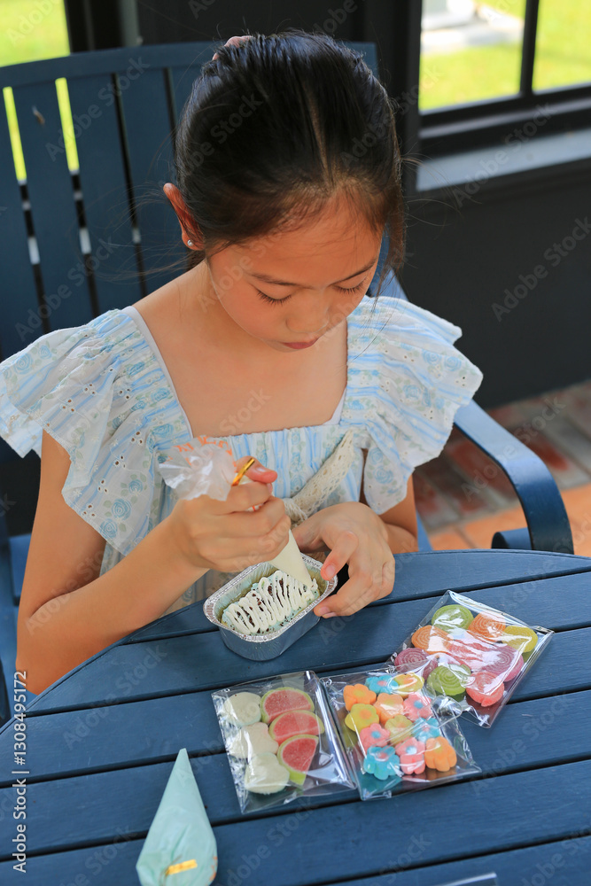 Asian girl child enjoy baking cake, decorating DIY cupcake.