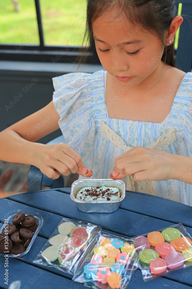 Asian girl child enjoy baking, decorating cupcake with jelly and icing sugar.