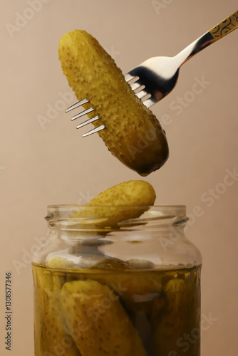 canned cucumbers in a transparent jar and one cucumber pricked on a fork