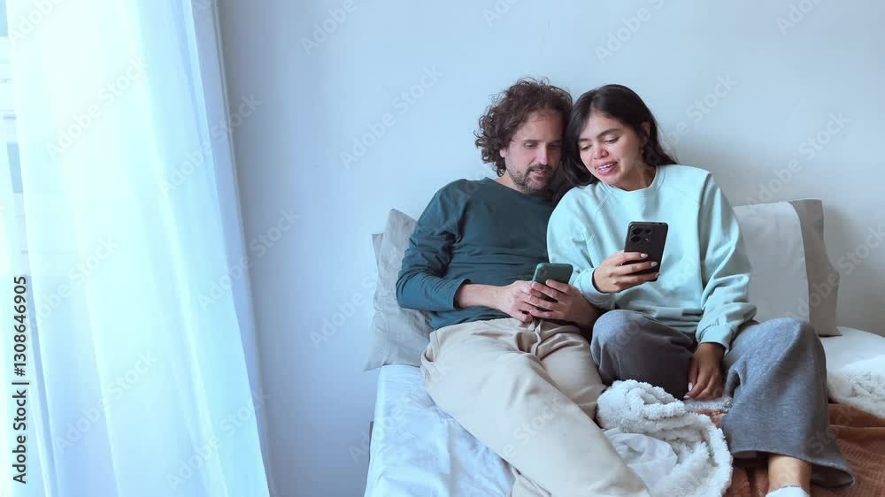 Couple laughing and using smartphone together in bed Couple laughing and using smartphone together in bed