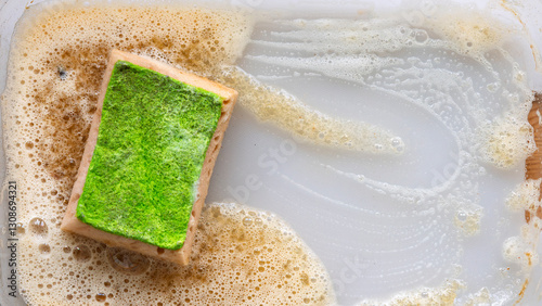 Fotografía A sponge with soap suds removes greasy stains from a plastic surface, leaving a clean area