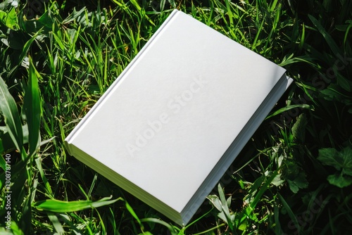  Mockup of white closed hardcover book on lush green grass. Minimalistic mockup for design and printing