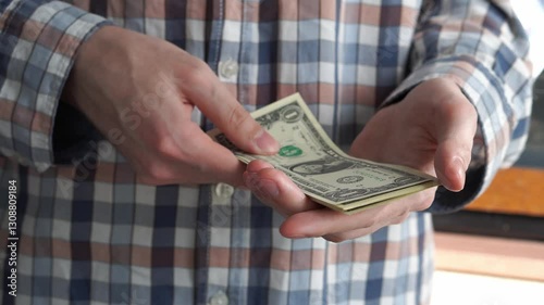 Male hands in plaid shirt counting dollar bills in a bundle close-up