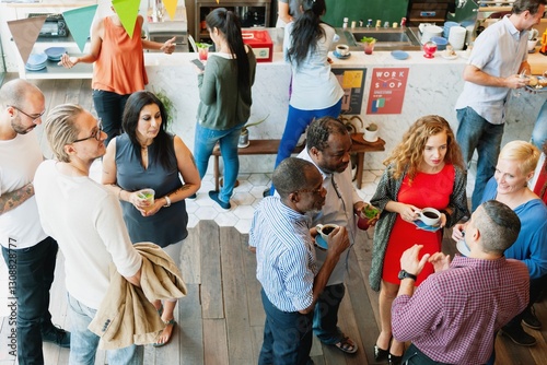 Diverse group socializing at a casual gathering. People chatting, holding drinks, and mingling at event. Indoor event with a mix of men and women. Diverse business people having coffee break.