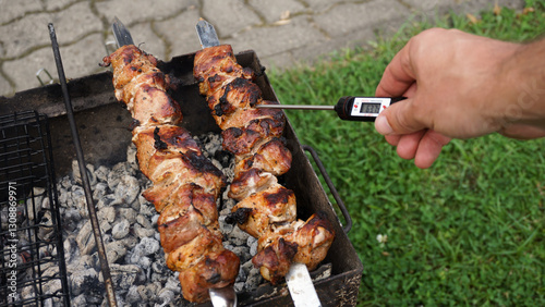 Man measuring meat temperature while grilling meat for outdoor barbeque in the backyard garden. Measuring food temperature with digital food thermometer.