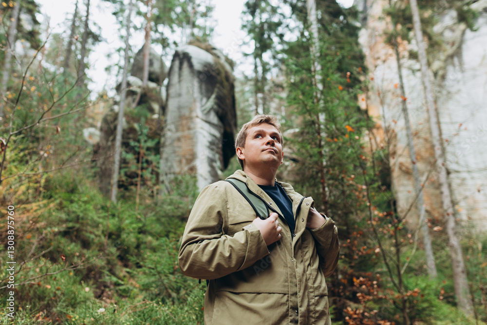 A tourist with a backpack stands against the background of a mountains and forest. Young 30s blonde man hiking in nature. Travel, adventure. Concept of an active lifestyle. High quality photo. A tourist with a backpack stands against the background of a mountains and forest. Young 30s blonde man hiking in nature. Travel, adventure. Concept of an active lifestyle. High quality photo.