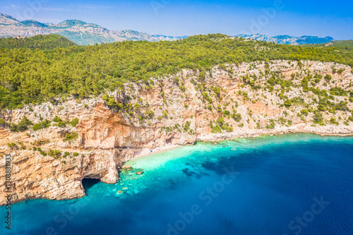 A breathtaking aerial view of Pasjaca Beach in Croatia, showcasing its secluded location beneath towering cliffs, golden sand, and the crystal-clear turquoise waters of the Adriatic Sea