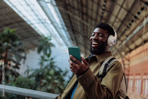 Tourist wearing headphones is using smart phone and smiling in airport or train station