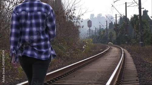 A young female traveler walking on railway tracks surrounded by nature. Tourism, freedom, and peace, walking along the rails in the greenery.Traveler on the railway tracks. solitude, adventure,harmony