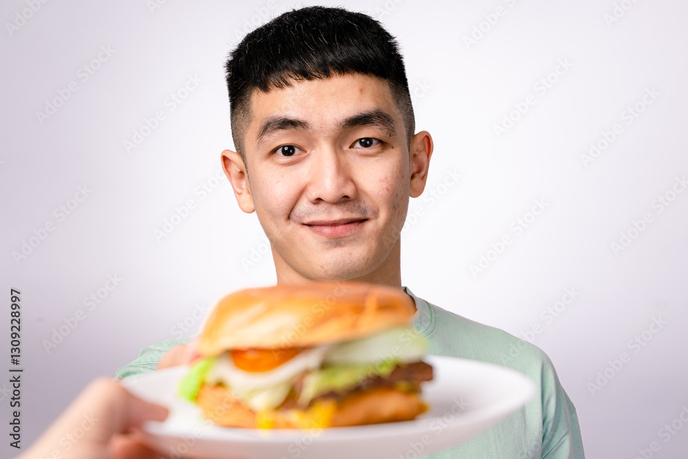 An Asian man in a mint green shirt excitedly presents a cheeseburger on a white plate. He has a wide smile, and the background is plain white An Asian man in a mint green shirt excitedly presents a cheeseburger on a white plate. He has a wide smile, and the background is plain white