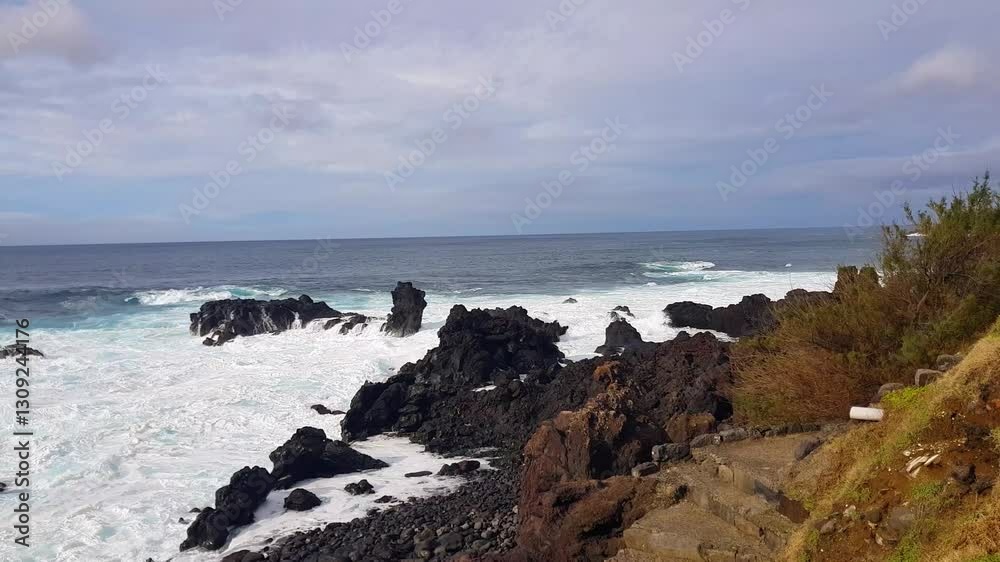 Scenic view of the wild, rugged coast of the Azores, where the Atlantic Ocean’s powerful waves crash against volcanic rocks beneath a cloudy sky Scenic view of the wild, rugged coast of the Azores, where the Atlantic Ocean’s powerful waves crash against volcanic rocks beneath a cloudy sky