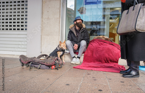 Homeless man with dog sitting on sidewalk and looking up while elegant woman is giving him alms