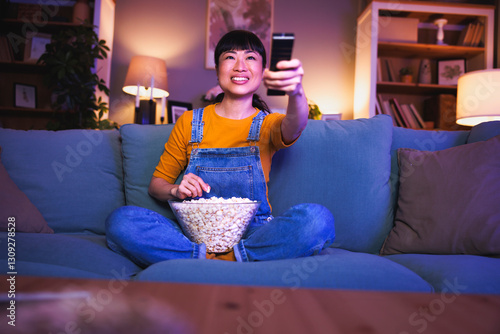 Woman turning up the volume on TV using remote control while relaxing at home late at night