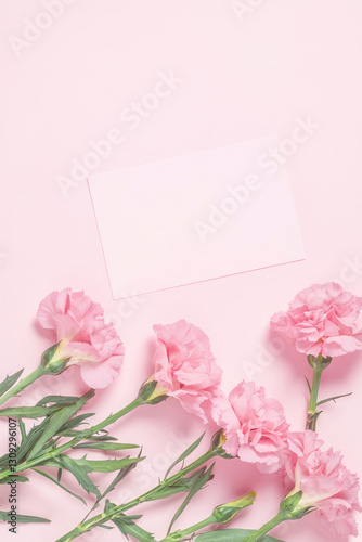Vertical Carnations pink background. Festive holiday greeting card for Birthday, Woman or Mothers Day, blank copy paper and a greeting card. View from above. Flat layout.