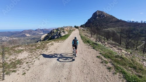 Cyclist rides gravel road, stunning mountain view.  Perfect for adventure, travel, and sports themes.  High-quality image for your projects.