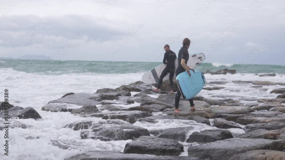 Slow motion, two surfers with boards are trying to enter the sea with waves on the rocks Slow motion, two surfers with boards are trying to enter the sea with waves on the rocks