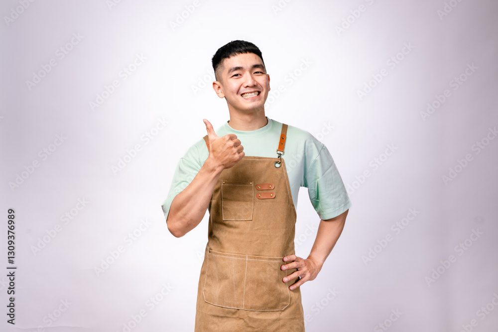 A cheerful Asian barista wearing a brown apron over a mint green shirt smiles while giving a thumbs-up against a white background. His confident and friendly pose conveys approval, satisfaction A cheerful Asian barista wearing a brown apron over a mint green shirt smiles while giving a thumbs-up against a white background. His confident and friendly pose conveys approval, satisfaction