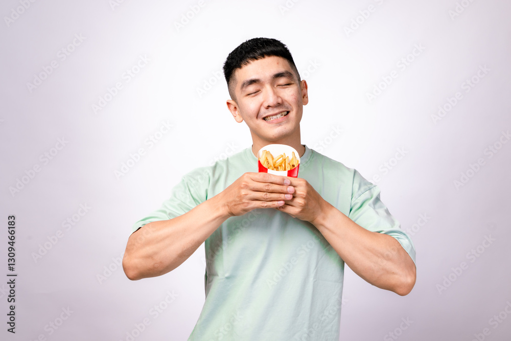An Asian man wearing a light green shirt holds a red container of French fries with both hands while smiling. He looks excited to eat. The background is white, and the fries appear crispy and golden An Asian man wearing a light green shirt holds a red container of French fries with both hands while smiling. He looks excited to eat. The background is white, and the fries appear crispy and golden