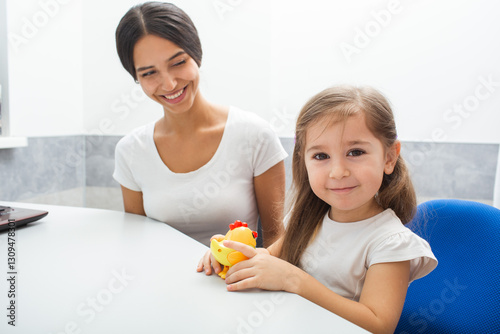 A young girl smiles while holding a toy during an occupational therapy session with her therapist in a cozy therapy room