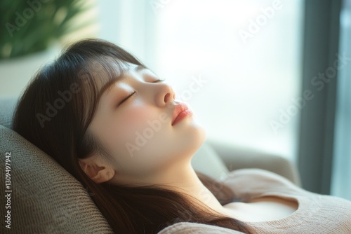 Free Download A young Asian woman with closed eyes, enjoying a moment of relaxation indoors. - GFXLoad