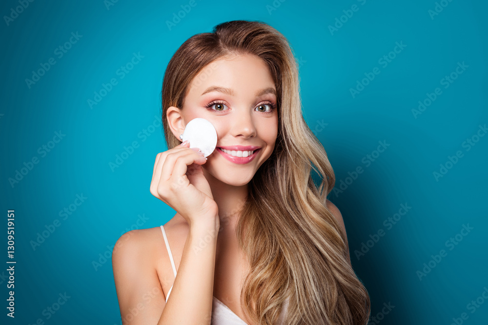 Beautiful young woman with flawless skin applying treatment pad while smiling against a vibrant blue background Beautiful young woman with flawless skin applying treatment pad while smiling against a vibrant blue background