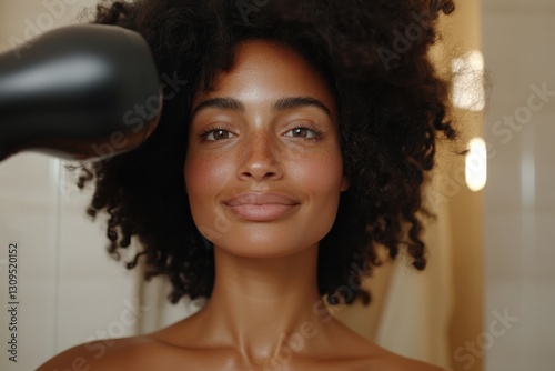 A cheerful woman drying her hair while smiling directly at the camera, portraying confidence and vitality in a bright bathroom setting, with soft lighting and warmth. photo