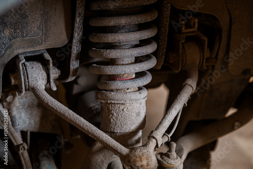 Close-up View of Dusty and Rusty Suspension System of Vehicle Showing Shock Absorber, Coil Spring, and Control Arms