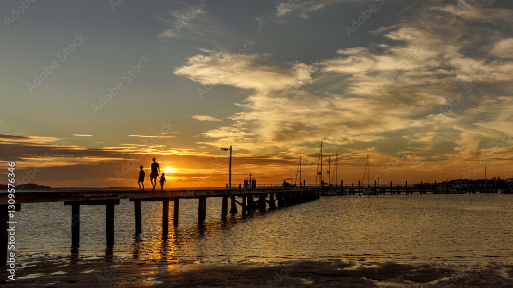 Silhouetted mother & her 2 daughters walking along wooden jetty at sunset Silhouetted mother & her 2 daughters walking along wooden jetty at sunset