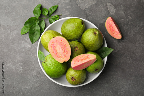 Fototapeta Naklejka Na Ścianę i Meble -  Fresh whole and cut guava fruits in bowl on grey textured table, top view