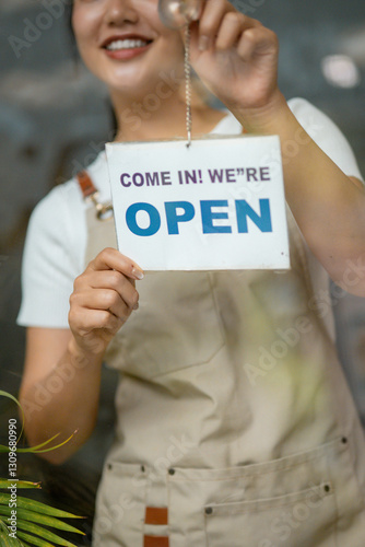 Friendly shopkeeper hanging open sign on glass door, welcoming potential patrons