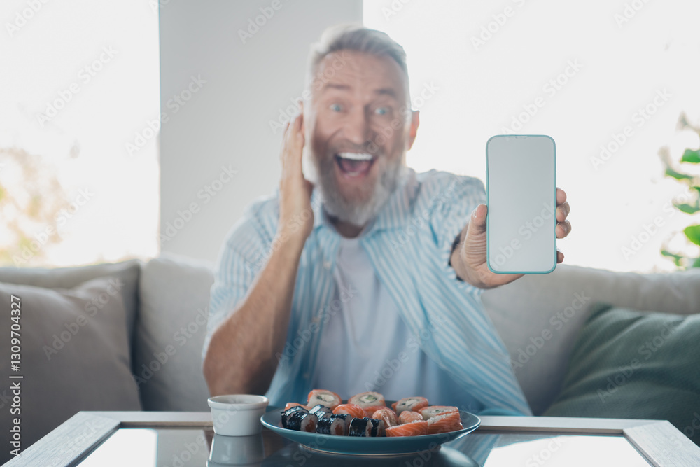 Elderly man joyfully showcasing smartphone while enjoying sushi at home during leisure time Elderly man joyfully showcasing smartphone while enjoying sushi at home during leisure time