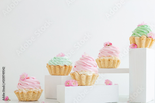 pink and green cupcakes with spring flowers  on wooden podiums on white  back...