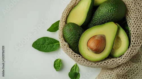 Fresh Avocados in a Reusable Bag With Green Leaves on a Light Background