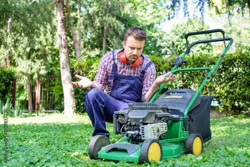 One guy portrait cutting the garden grass having problem with the lawn mower
