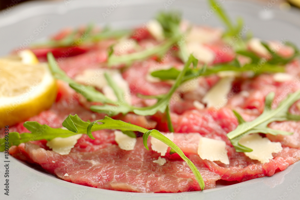 Fresh beef carpaccio with arugula, cheese and lemon on plate, closeup Fresh beef carpaccio with arugula, cheese and lemon on plate, closeup