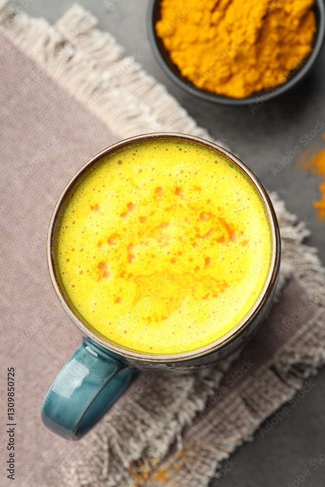 Tasty turmeric latte in cup and powder on grey table, flat lay