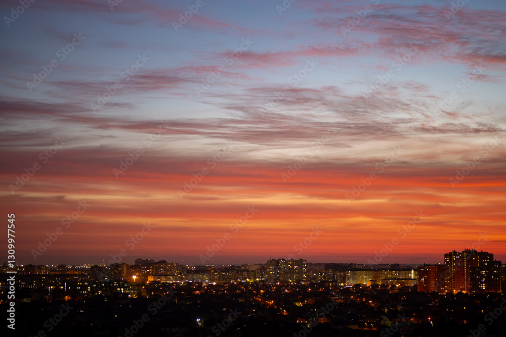 City skyline at sunset with dark building silhouettes against a sky with orange, red, and purple clouds. Urban evening landscape with illuminated windows City skyline at sunset with dark building silhouettes against a sky with orange, red, and purple clouds. Urban evening landscape with illuminated windows