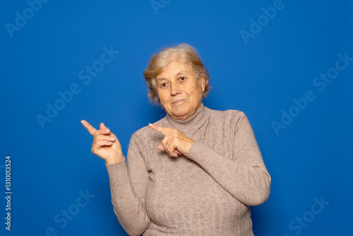 Caucasian woman about 70s wearing casual winter sweater smiling and looking at the camera pointing with two hands and fingers to the side. Isolated on blue background